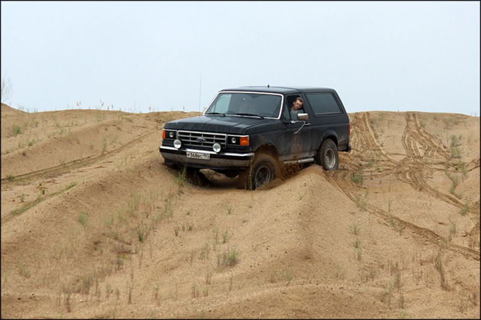 Black 1987 Ford Bronco climbing a sand dune with tire tracks visible