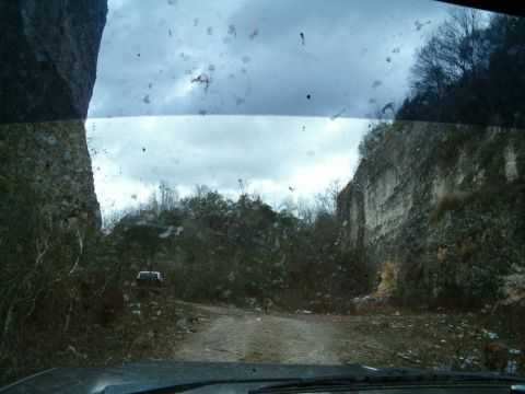 1991 Ford Bronco - View from inside a vehicle looking out at a white SUV on a dirt road within a rocky quarry landscape.