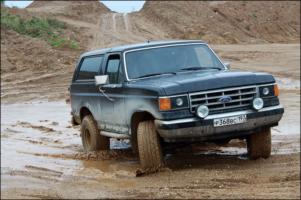 Black 1987 Ford Bronco driving through mud