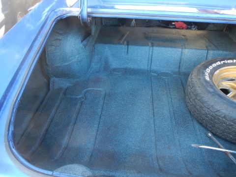1967 Pontiac GTO - The trunk of a blue car shows its carpeted interior and a spare tire with a gold rim.