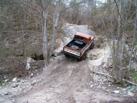 1991 Ford Bronco - Rear three-quarter view of an orange-and-white lifted 1970s Ford 4x4 pickup with FORD-lettered tailgate and a spare tire in the bed, nosed…