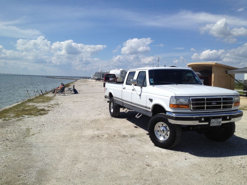 1997 Ford F-350 pickup truck parked by the water with fishing rods and campers in the background. License plate reads BYT-7509