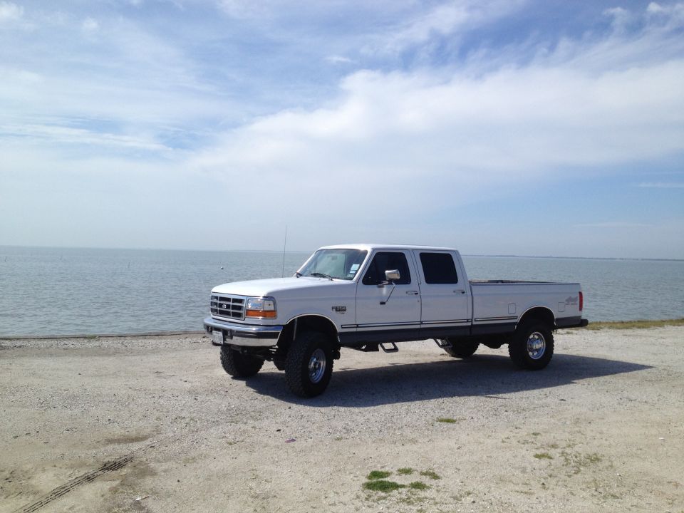 White 1997 Ford F-350 crew cab pickup truck parked on a gravel lot near the water
