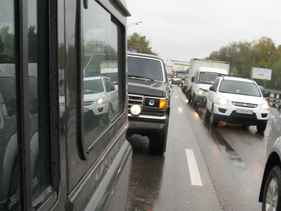 Black 1987 Ford Bronco in traffic, front view, with a round headlight on the driver's side
