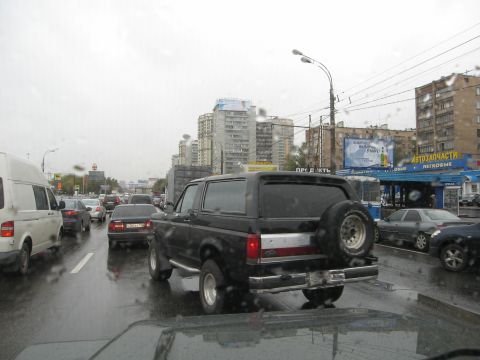 1987 Ford Bronco - A black 1987 Ford Bronco is seen from behind in traffic on a rainy day.