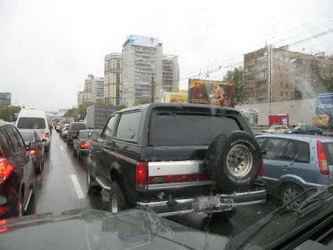 1987 Ford Bronco - A black Ford Bronco is seen in heavy traffic on a wet day, with buildings in the background.
