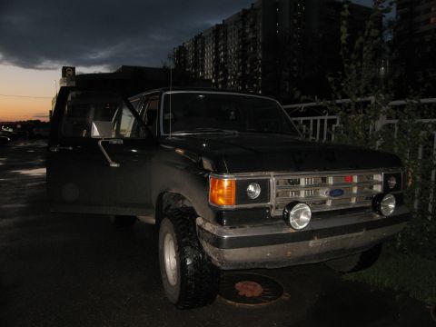 1987 Ford Bronco - Black 1987 Ford Bronco with driver door open, parked at dusk with apartment buildings in the background.