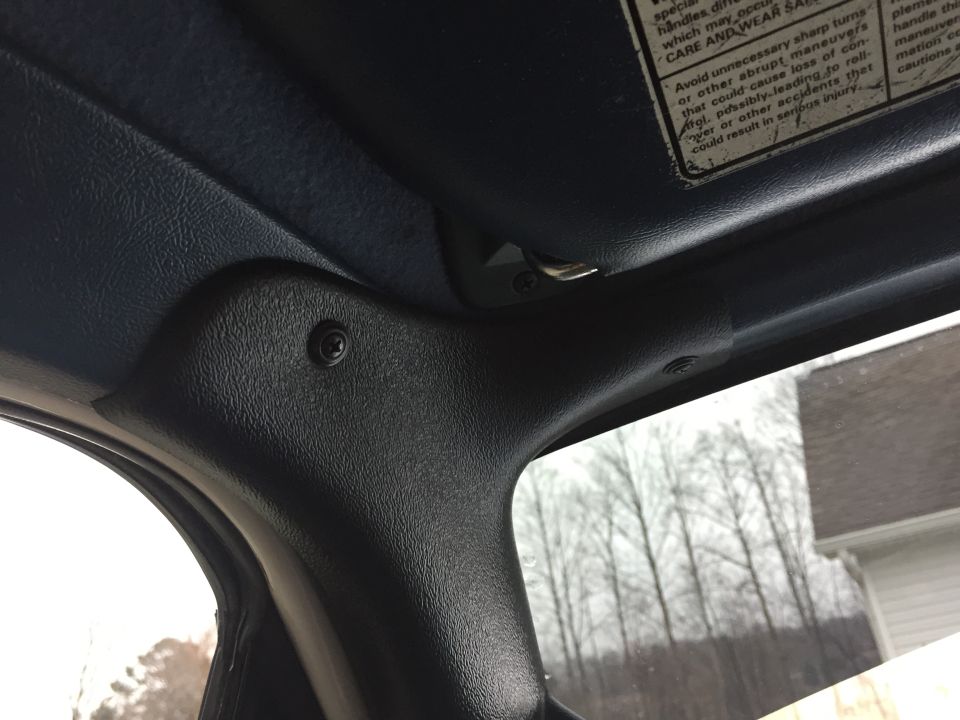 Interior view of a vehicle's A-pillar and visor clip, with a warning label visible on the visor
