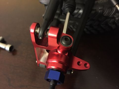 2014 Dodge 1500 - Close-up of a red aluminum steering knuckle assembly, a blue nut and visible suspension components.