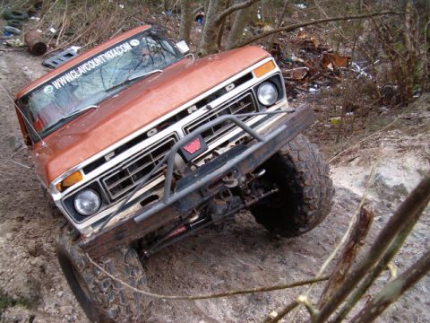 1991 Ford Bronco - This orange 1977 Ford F-Series truck navigates a muddy, off-road trail with a custom front bumper and large tires.