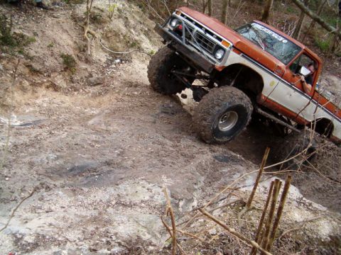 1991 Ford Bronco - An orange-and-white 1970s Ford full-size 4x4 on a solid-axle lift with oversized mud-terrain tires and chrome wheels crawls down a steep, w…