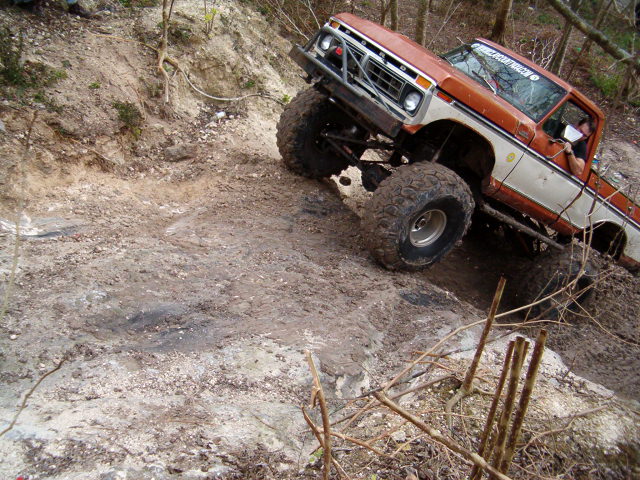 Lifted orange and white 1970s Ford 4x4 on big mud tires crawling down a wet clay bank