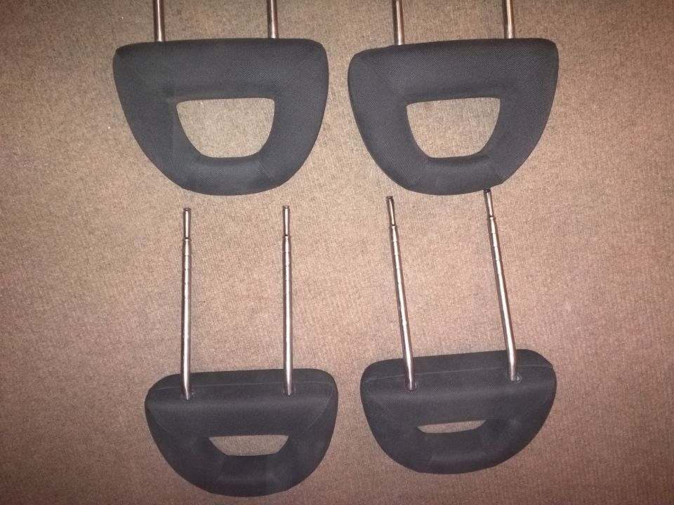 Four black car headrests with metal posts, laid out on a carpeted surface