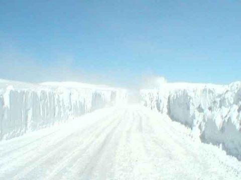 1979 Ford Bronco - A road is barely visible between towering walls of snow under a clear blue sky.