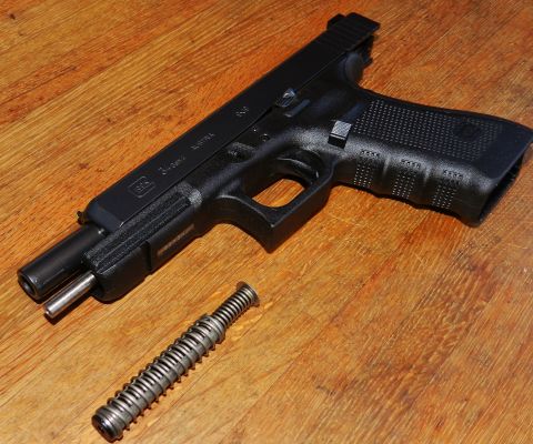 1996 Ford Bronco - A disassembled Glock pistol lies on a wooden surface, with its recoil spring assembly separate.