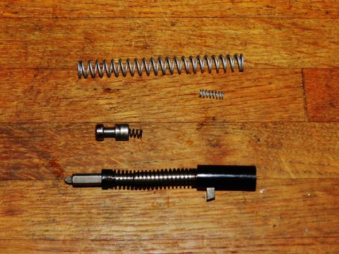 1996 Ford Bronco - Disassembled gun parts, including a barrel, springs, and a pin, are laid out on a wooden surface.