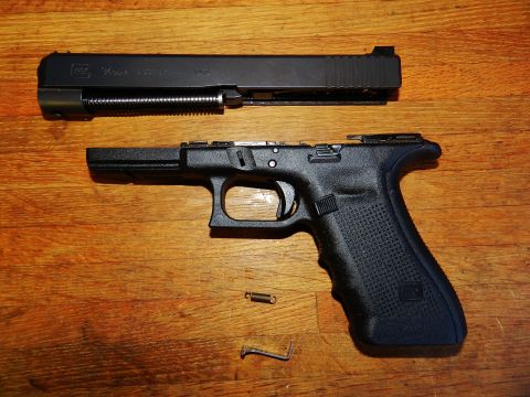 1996 Ford Bronco - A disassembled Glock handgun lies on a wooden table, with its slide and frame separated.