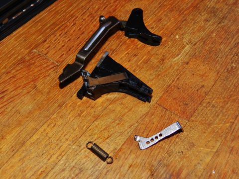 1996 Ford Bronco - Disassembled gun trigger mechanism and spring lie on a wooden surface.