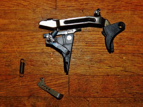 1996 Ford Bronco - Disassembled gun trigger mechanism, including a spring and lever, laid out on a wooden surface. A part number is visible on the assembly.