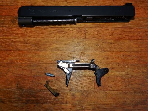 1996 Ford Bronco - Disassembled Glock pistol slide and trigger assembly laid out on a wooden surface.