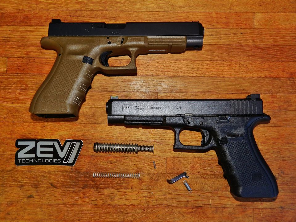 Two Glock pistols, one tan and one black, disassembled with parts laid out on a wooden surface. A ZEV Technologies logo is visible