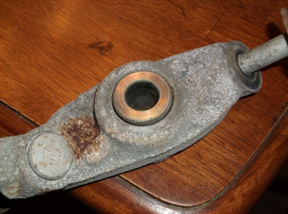 Close-up of a metal suspension control arm with a brass bushing. A bolt is visible on the left