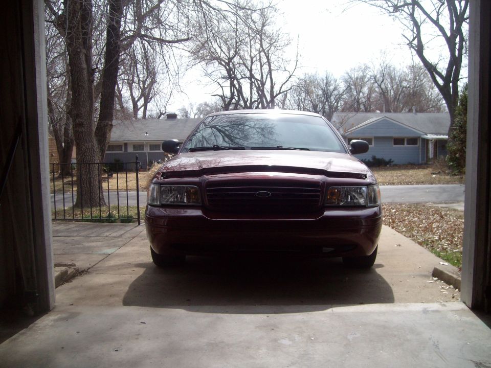 Maroon Ford Crown Victoria parked in a garage, front view. Hood is slightly ajar
