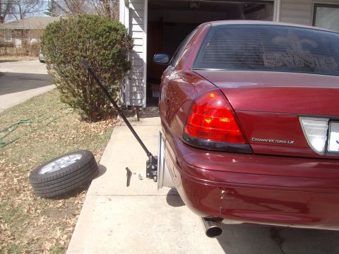 2004 Ford Crown Victoria - A flat tire is being changed on a maroon Ford Crown Victoria LX in front of a garage.
