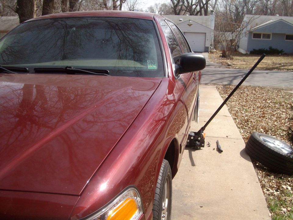 Red 2004 Ford Crown Victoria with a jack under the front passenger side, flat tire removed