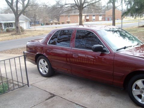 2004 Ford Crown Victoria - A maroon sedan is parked on a concrete driveway in front of a residential house.