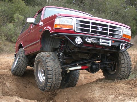1996 Ford Bronco - Modified 1996 Ford Bronco navigating an off-road obstacle with its front wheels elevated.