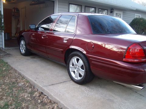 2004 Ford Crown Victoria - A maroon sedan is parked on a concrete driveway in front of a garage.