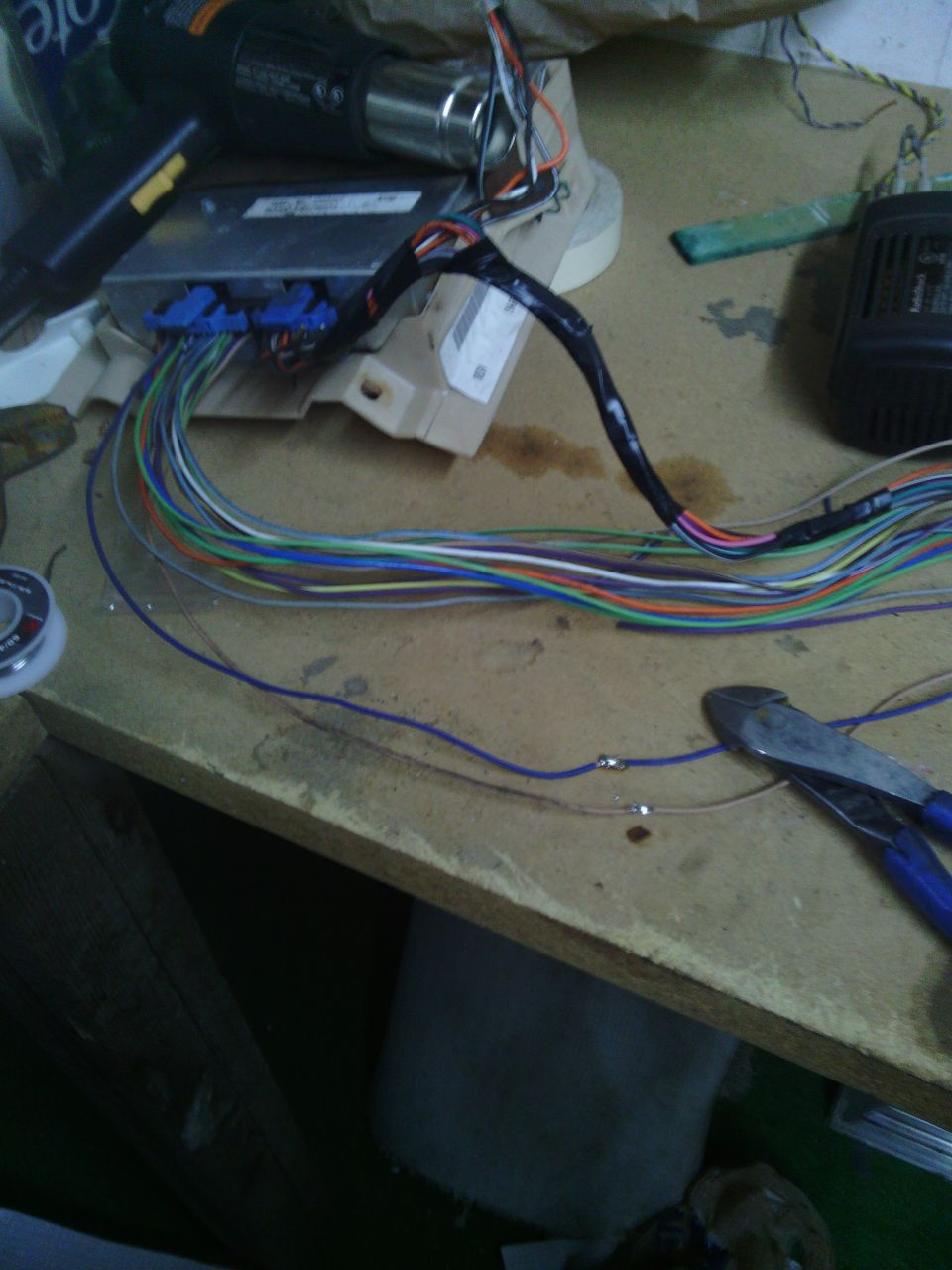 Wiring harness connected to an electronic control unit on a wooden surface, with wire cutters nearby