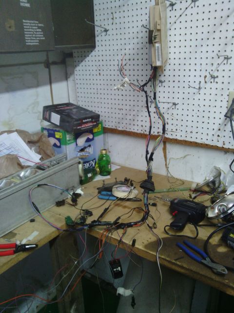 1978 Ford Bronco - Workbench cluttered with a disassembled vehicle wiring harness, tools, and parts.