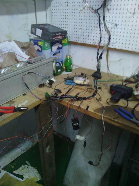1978 Ford Bronco - A complex vehicle wiring harness is laid out on a workbench, surrounded by tools and supplies.