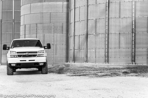 2006 Chevrolet Silverado 2500 - A white pickup truck is parked in front of large, industrial silos.