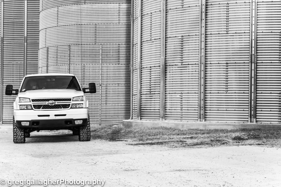 White pickup truck parked in front of large corrugated metal silos