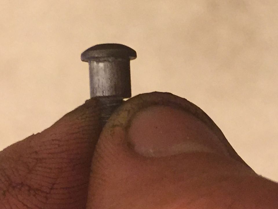 Fingers holding a small metal rivet or pin