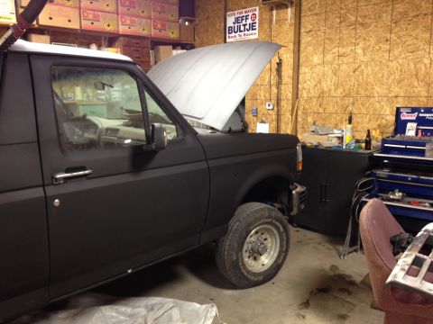 1992 Ford Bronco - A black Ford Bronco sits in a garage with its hood open, surrounded by tools and storage.