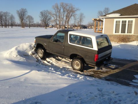 1992 Ford Bronco - A dark gray and white Ford Bronco navigates a snowy driveway on a clear winter day.