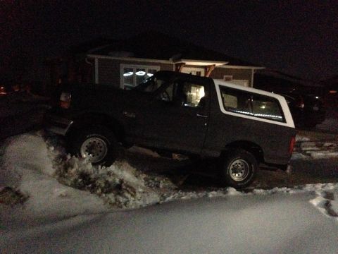 1992 Ford Bronco - A 1992 Ford Bronco navigates a snowy area at night, with a house in the background.