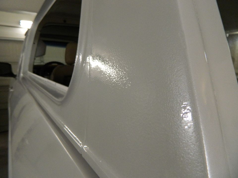 Close-up of a white vehicle's side panel with a textured finish. Interior visible through the window