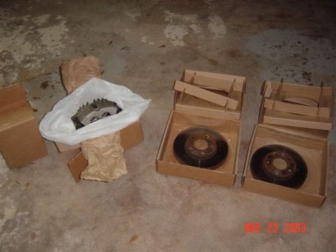 1999 Ford Mustang - New brake rotors and caliper are laid out on a concrete floor, ready for installation.