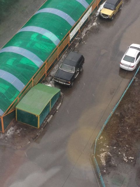 1987 Ford Bronco - A black SUV is parked next to a covered walkway, with other vehicles nearby on a wet day.