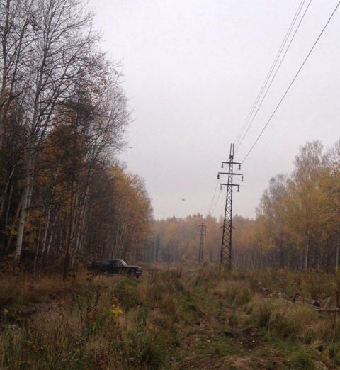 1987 Ford Bronco - A lone SUV sits parked in a field surrounded by trees in autumn, with tall power line towers in the background.