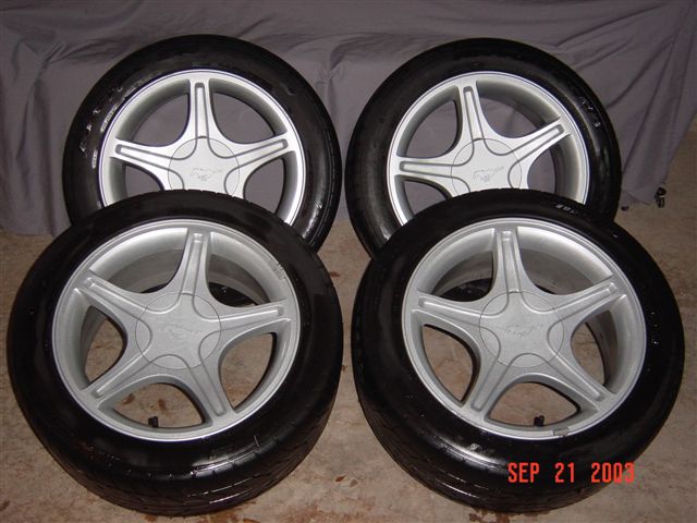 four silver 5-spoke wheels with black tires, each center cap has a horse emblem