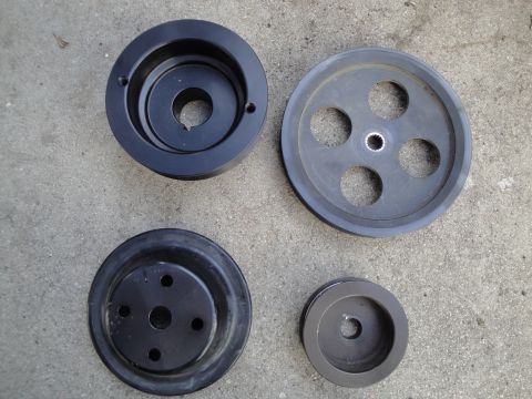 1995 Ford Taurus - A collection of engine pulleys, including a large one with multiple holes and a smaller, darker one, are displayed on a rough concrete back…