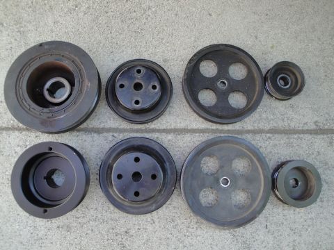 1995 Ford Taurus - A collection of various automotive drive pulleys laid out on a concrete surface.