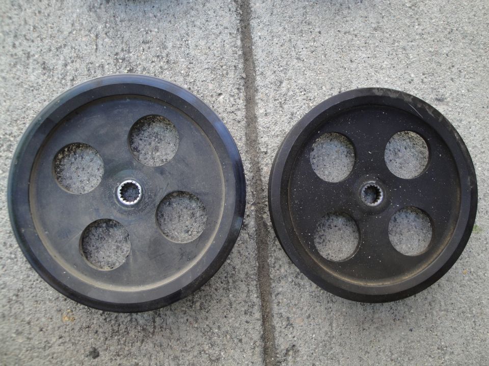 Two black drive pulleys with circular cutouts sit on a concrete surface