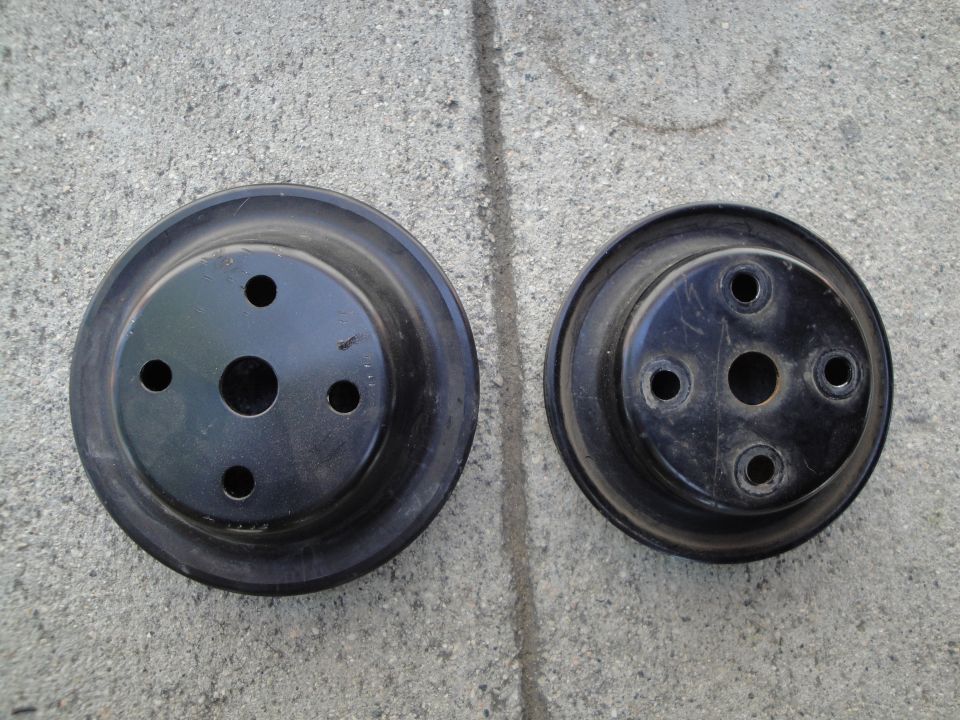 Two black automotive pulleys with circular mounting holes, resting on a concrete surface